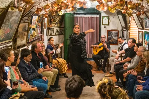 Artistas flamencos de Granada actúan en un tablao íntimo, con una bailaora en primer plano y un guitarrista acompañando.
