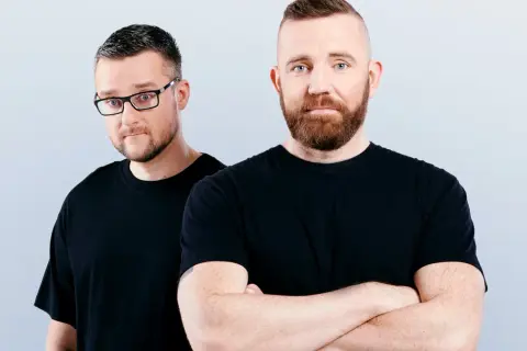 Dwóch mężczyzn w czarnych koszulkach, jeden w okularach, drugi ze skrzyżowanymi rękami. Wyglądają jak duet Catz n Dogz.