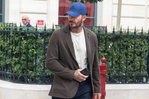 Uomo con abbinamento blu e marrone: blazer marrone, t-shirt bianca, cappellino blu e pantaloni scuri.
