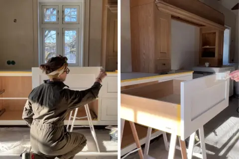 Person målar furu köksluckor vita. Solen lyser in genom fönstret och skapar skuggor.