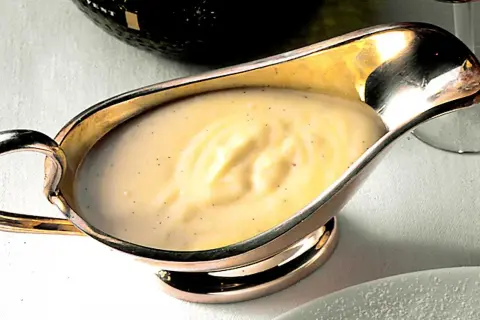 Krämig vaniljsås med små prickar av vaniljsocker i en elegant silverkanna, redo att serveras.