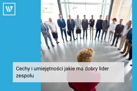 Grupa ludzi w garniturach stoi w kręgu, słuchając swojego **team leadera**.