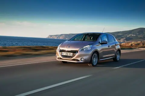 En Peugeot 208 kör längs en kustväg med havet till vänster och berg i bakgrunden. En perfekt bild för ett peugeot 208 test.