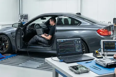 Taller de **que es tuning**: un coche en banco de potencia, un técnico en el asiento con portátil y otro soldando una centralita.