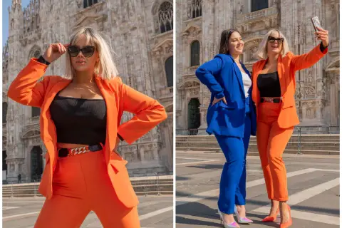 Dwie kobiety w eleganckich garniturach, jedna w intensywnym niebieskim, druga w żywym pomarańczowym kolorze, pozują przed katedrą.