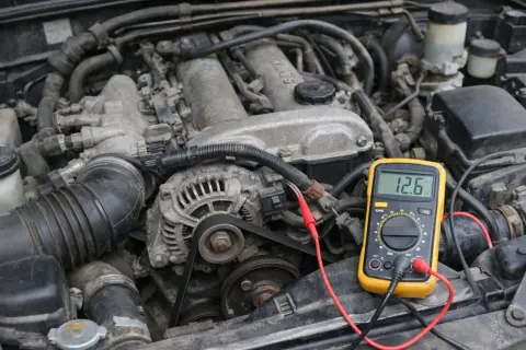 Un multimètre jaune connecté à un alternateur de voiture pour tester son fonctionnement. La lecture indique 12.6V.