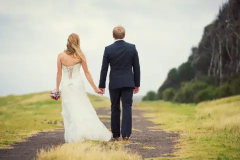 Un couple de jeunes mariés se promène main dans la main sur un chemin, un bouquet à la main. Un beau mariage au mois de mai.