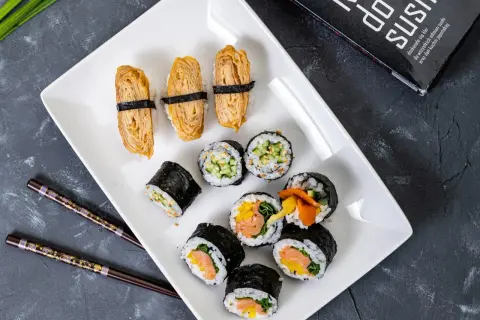 Pyszne domowe sushi przepis na talerzu: nigiri z omletem tamago, rolki z łososiem i warzywami, ogórkiem i sezamem.