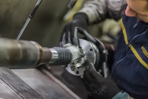 Mechanik w rękawiczkach montuje przegub wału kardana.