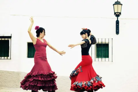 Dos mujeres bailan flamenco, con faldas rojas y volantes. Una lección de baile flamenco para principiantes.