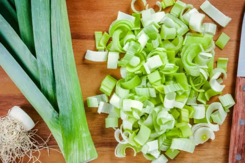 Frischer Lauch, bereit für leckere porree rezepte. Ganze Stangen und fein geschnittene Ringe liegen auf einem Holzbrett.