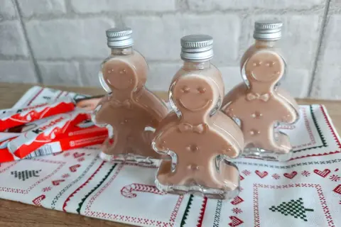 Trzy buteleczki likieru w kształcie ludzików z piernika, obok batoniki Kinder.