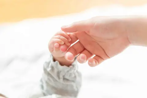 Delikatny chwyt pęsetkowy małego paluszka niemowlęcia przez dorosłą dłoń.