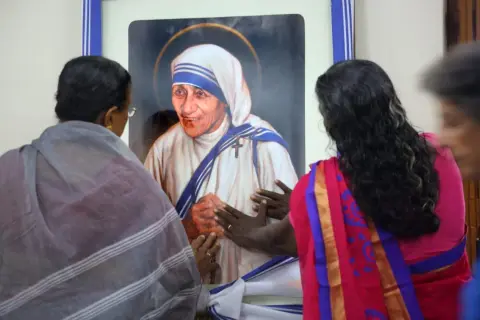 Frauen berühren ein Bild von Mutter Teresa, die ihr Leben den Armen widmete.