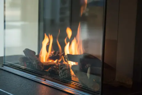 Flammen tanzen um Holzscheite in einem modernen Kamin. Ein Blick, der zeigt, wie man Ascheflecken entfernen kann, ohne die Gemütlichkeit zu stören.
