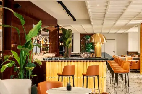 Interni eleganti del Bulgari Hotel Roma: bancone bar dorato, sedie in pelle arancione, piante lussureggianti e un'atmosfera sofisticata.