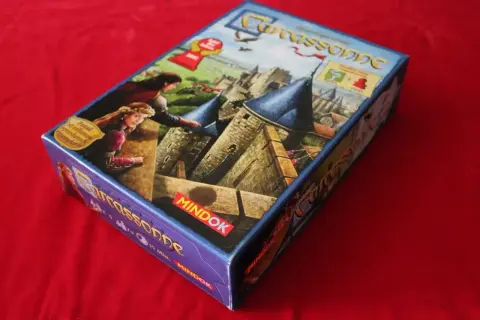 Pudełko gry planszowej Carcassonne, z motywem zamku i postaci, sugeruje nowe **carcassonne rozszerzenia**.