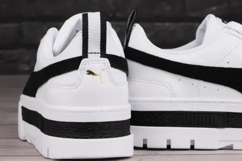 Białe buty sportowe Puma Mayze Leather z czarnymi akcentami i złotym logo. Gruba podeszwa dodaje im charakteru.