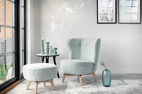 En bekväm fåtölj i turkos nyans, med en matchande pall och en blå vas med blommor.