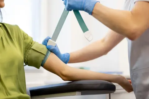 Pielęgniarka zakłada opaskę uciskową na ramię pacjentki przed pobraniem krwi. Badanie progesteronu jest ważne dla oceny zdrowia reprodukcyjnego.