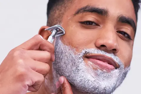 Uomo con schiuma da barba aggrappante prima della rasatura, mentre usa un rasoio di sicurezza.