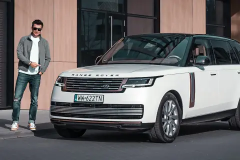 Elegancki mężczyzna obok białego Range Rovera. Sprawdź aktualną range rover cena i dowiedz się więcej o tym luksusowym SUV-ie.