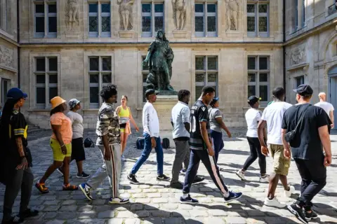 Un groupe de jeunes explore les musées de Paris, admirant une statue devant un bâtiment historique.