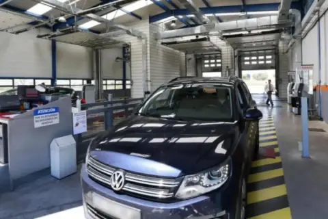 Un coche oscuro en un centro de inspección técnica, listo para pasar la ITV. El personal revisa los papeles.