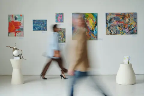 W galerii sztuki, gdzie obrazy zachęcają do kreatywności, jak w muzeum dla dzieci, dwie postacie w ruchu podziwiają abstrakcyjne dzieła.