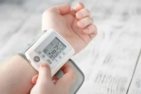 Dłoń z założonym ciśnieniomierzem nadgarstkowym pokazującym wynik 145/87 mmHg i puls 46/min.
