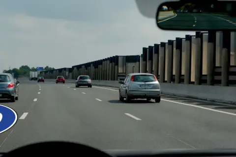 Panneau de signalisation au sol indiquant la vitesse minimale autoroute de 80 km/h. Plusieurs voitures circulent sur la voie rapide.