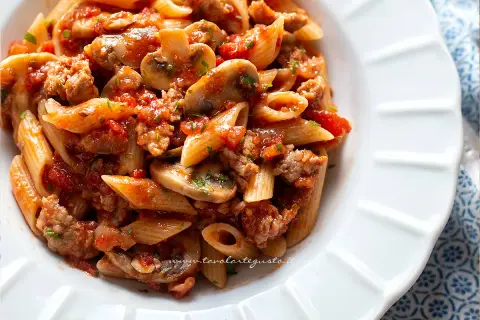 Piatto di pasta alla boscaiola con penne, funghi, salsiccia e pomodoro, un classico saporito.