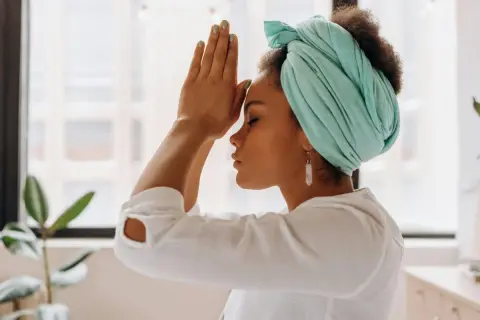 Mujer con turbante turquesa y pendientes largos medita. A veces, cuando me enfado y no respiro, busco la calma así.
