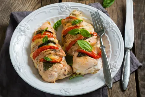 Pyszna pierś z kurczaka z suszonymi pomidorami i mozzarellą z piekarnika, udekorowana świeżą bazylią.