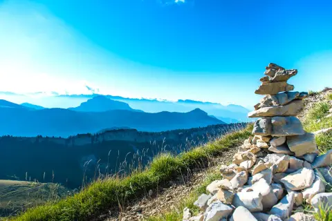 Un cairn de pierres marque le sommet, offrant une vue panoramique sur la grande sure et les montagnes bleutées à perte de vue sous un ciel clair.