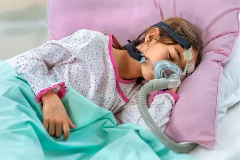 Dziecko śpi z maską CPAP, która pomaga mu oddychać podczas snu, łagodząc bezdech u dziecka.