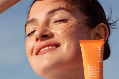 Une jeune femme rayonne sous le soleil, protégeant sa peau avec un fluide solaire. Un rappel : mettre de la crème solaire tous les jours pour une peau éclatante.