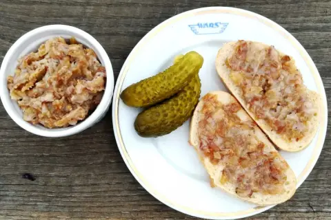 Smalec z cebulą i jabłkiem w miseczce, na talerzu kromki chleba ze smalcem i ogórki kiszone.