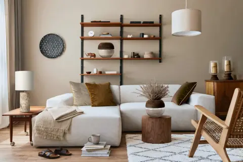Przytulny salon boho inspiracje: jasna kanapa, drewniane meble, pleciony fotel, dywan i dekoracje tworzą ciepłą atmosferę.