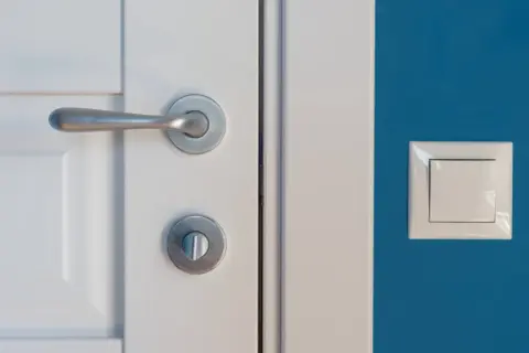 Stalowe klamki do białych drzwi idealnie komponują się z niebieską ścianą i białym włącznikiem.