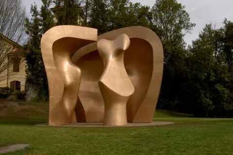 Escultura abstracta dorada en el parque de los pueblos de Europa, con formas curvas y orgánicas, rodeada de césped y árboles frondosos.