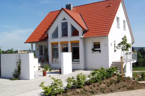 Nowy biały dom z czerwonym dachem, z widoczną odległością budynku od drogi wewnętrznej.