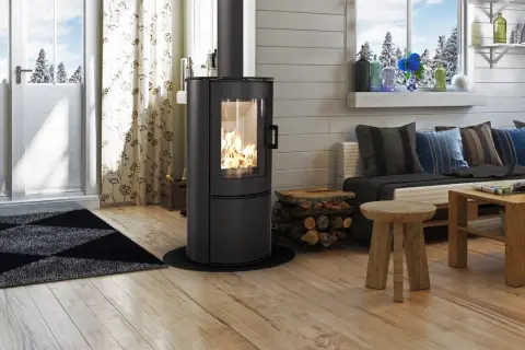 Gemütliches Wohnzimmer mit brennendem Kaminofen (BimschV Stufe 2 Liste), Holzstapel, Sofa mit Kissen und Holztisch.