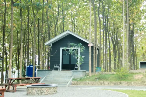 Mały, ciemny domek letniskowy w lesie, z kamiennym paleniskiem i ławką. Idealne miejsce na wypoczynek, z solidnymi bloczkami pod domek letniskowy.