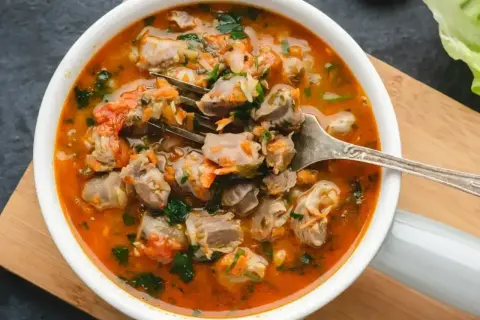 Aromaticzny, tradycyjny gulasz z żołądków drobiowych z warzywami i ziołami, podany w białej misce.