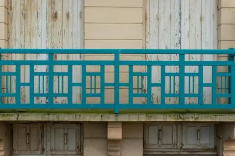 Turkusowe, geometryczne mocowanie balustrady od czoła, z widocznymi odrapanymi drzwiami poniżej.