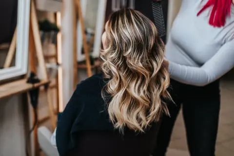 Fryzjerka kończy stylizację włosów klientki, tworząc efekt baleyage a sombre.
