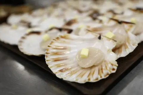 Coquilles Saint-Jacques prêtes à être cuisinées, chacune garnie d'un cube de beurre.