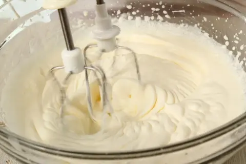 Ubity krem śmietankowy do tortu bez mascarpone, przygotowywany mikserem w szklanej misie.