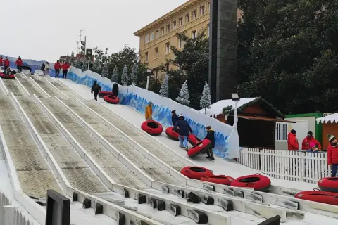 Diversión en los trineos de la Plaza del Pilar. Niños y adultos disfrutan de un tobogán nevado, con la Basílica de Nuestra Señora del Pilar de fondo.